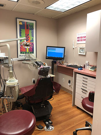 The image depicts a dental office setup with a dental chair, a computer monitor displaying a patient s X-ray, and various dental equipment.
