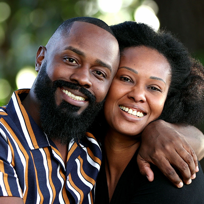 A man and woman are hugging each other closely, smiling warmly at the camera.